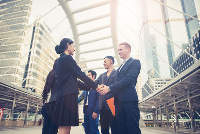 Business people giving handshake while standing against building in city