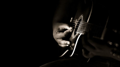 Cropped image of man playing guitar against black background