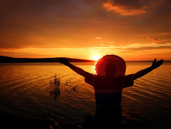 Rear view of silhouette people in sea against sky during sunset