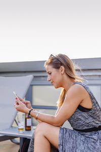 Side view of young woman using smart phone against sky