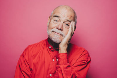 Portrait of bored senior man with head in hand against pink background