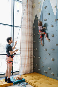 Young boy indoor rock climbing with his father instructor. hobby or home sport concept