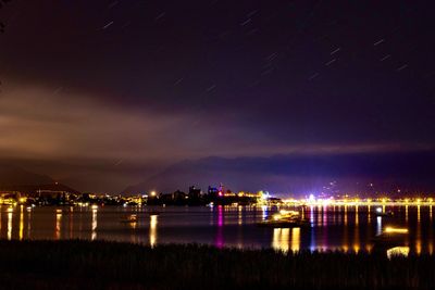 Illuminated buildings by river against sky at night