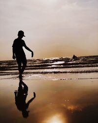 Silhouette man standing on beach against sky during sunset