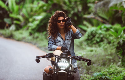 Woman holding sunglasses while sitting on motor bike