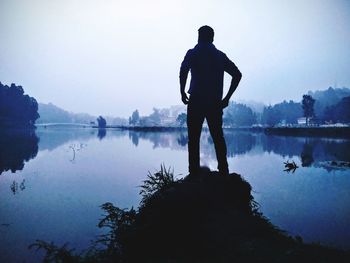 Rear view of man looking at lake against sky