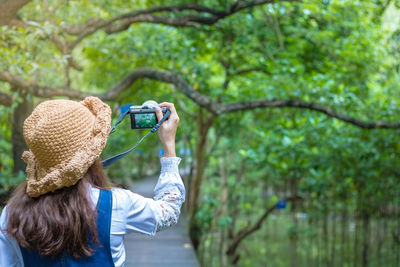 Rear view of woman photographing camera on tree