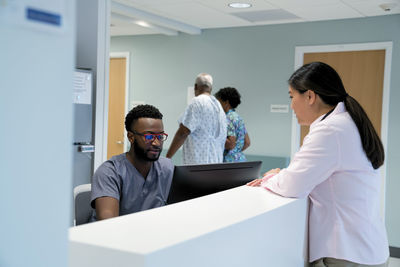 Doctor talking to male nurse at hospital reception while colleague with patient walking in background