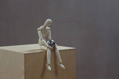 Close-up of wooden figurine with metallic ball on table against wall