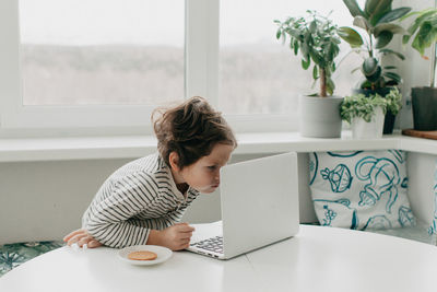 Little boy siting at the kitchen and look at the laptop. high quality photo