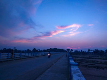 Road by city against sky during sunset