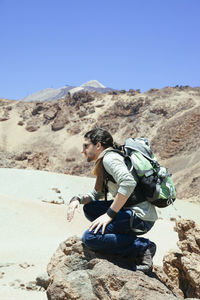 Side view of man on rock against sky