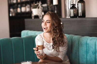 Smiling young woman holding coffee cup at cafe