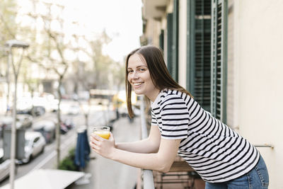 Portrait of smiling young woman holding drink in city