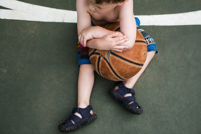 High angle view of boy holding basketball while sitting on court