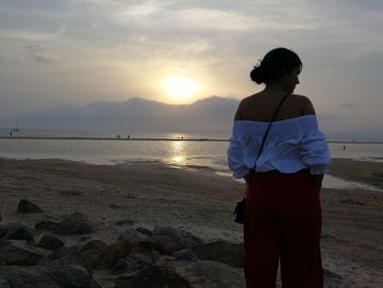 Rear view of woman standing against sea during sunset