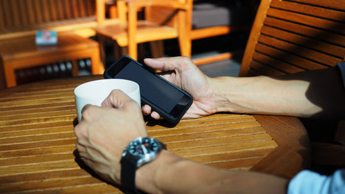 Cropped hands using phone while holding coffee cup at table