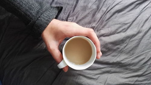Cropped image of person holding coffee on bed