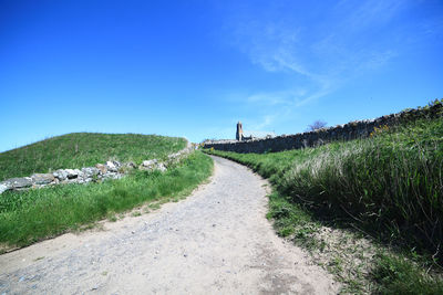 Road amidst field against clear blue sky