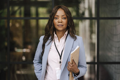 Confident female entrepreneur standing with file in front of glass wall at convention center