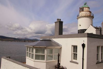 Lighthouse by buildings against sky