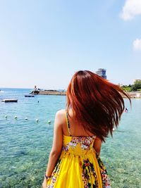 Rear view of woman standing at beach against clear sky