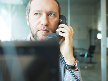 Businessman looking away while talking on landline phone at office