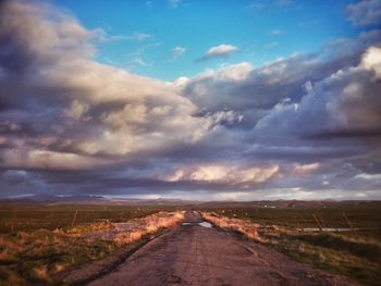 Road passing through field against cloudy sky