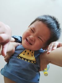 Cropped hands of mother holding cute smiling son against wall