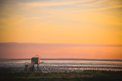 Scenic view of sea and fishing hut against orange sky