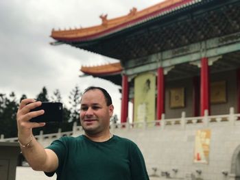 Man taking selfie through mobile phone while standing against temple