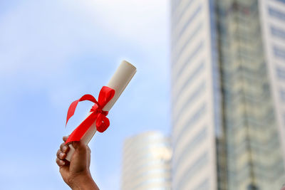 Low angle view of hand holding rolled paper against building in city