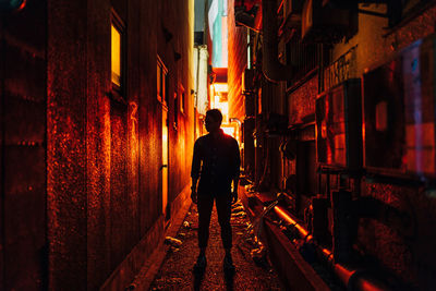 Rear view of man walking on alley amidst buildings at night