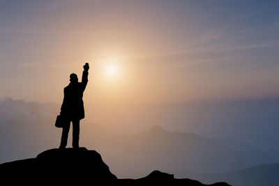 Silhouette man standing on rock against sky during sunset