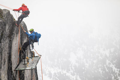 Climbers rappelling onto portaledge on a vertical cliff face.