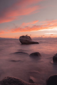 View of rock in sea against sky during sunset