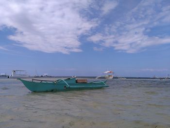 Boats moored in calm sea against cloudy sky