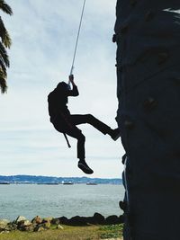 Full length of person climbing on rock by sea against sky