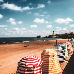 Hooded chairs on beach against sky