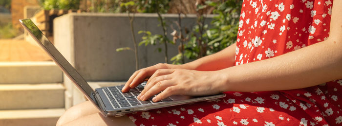 Unrecognizable young woman in red dress working on laptop. freelancer's place of work. study and