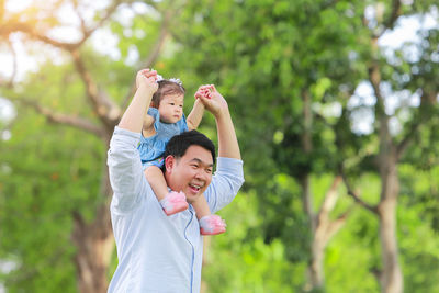 Smiling father piggybacking daughter against trees