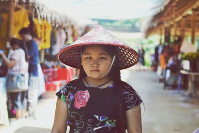 Portrait of girl wearing asian style conical hat while standing at market