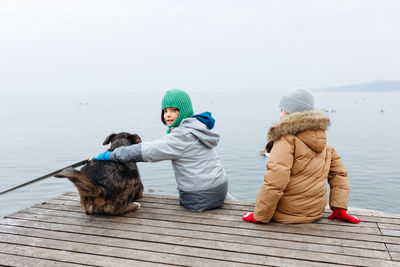 Rear view of woman sitting on pier over sea against clear sky