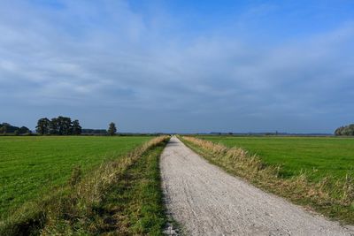 Dirt road amidst field against sky