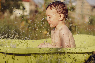 Cute little boy bathing in tub outdoors in garden. happy child is splashing, playing with water 