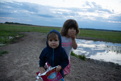 Portrait of siblings standing by pond against sky