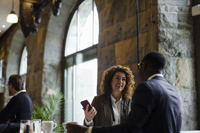 Smiling businesswoman with smart phone talking with male entrepreneur at seminar