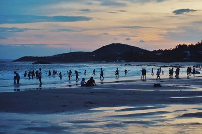 Group of people on beach against sky during sunset