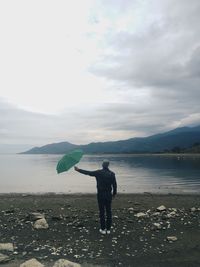 Rear view of man standing at beach against sky