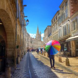 Rear view of man with multi colored umbrella walking on city street